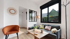 A modern living room with a sofa, a chair, a coffee table, and a window with a view of a garden. - Chalet at the Gates of Goulet (Plouzané)