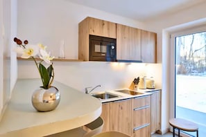 A modern kitchen with wooden cabinets, a built-in microwave, and a large window providing a view of the outdoors. - Deluxe Single with Kitchenette (Starnberg)
