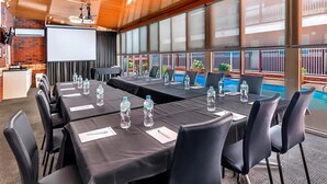 Ein Konferenzraum mit einer großen Leinwand, mehreren Tischen mit Stühlen und Blick auf einen Swimmingpool.