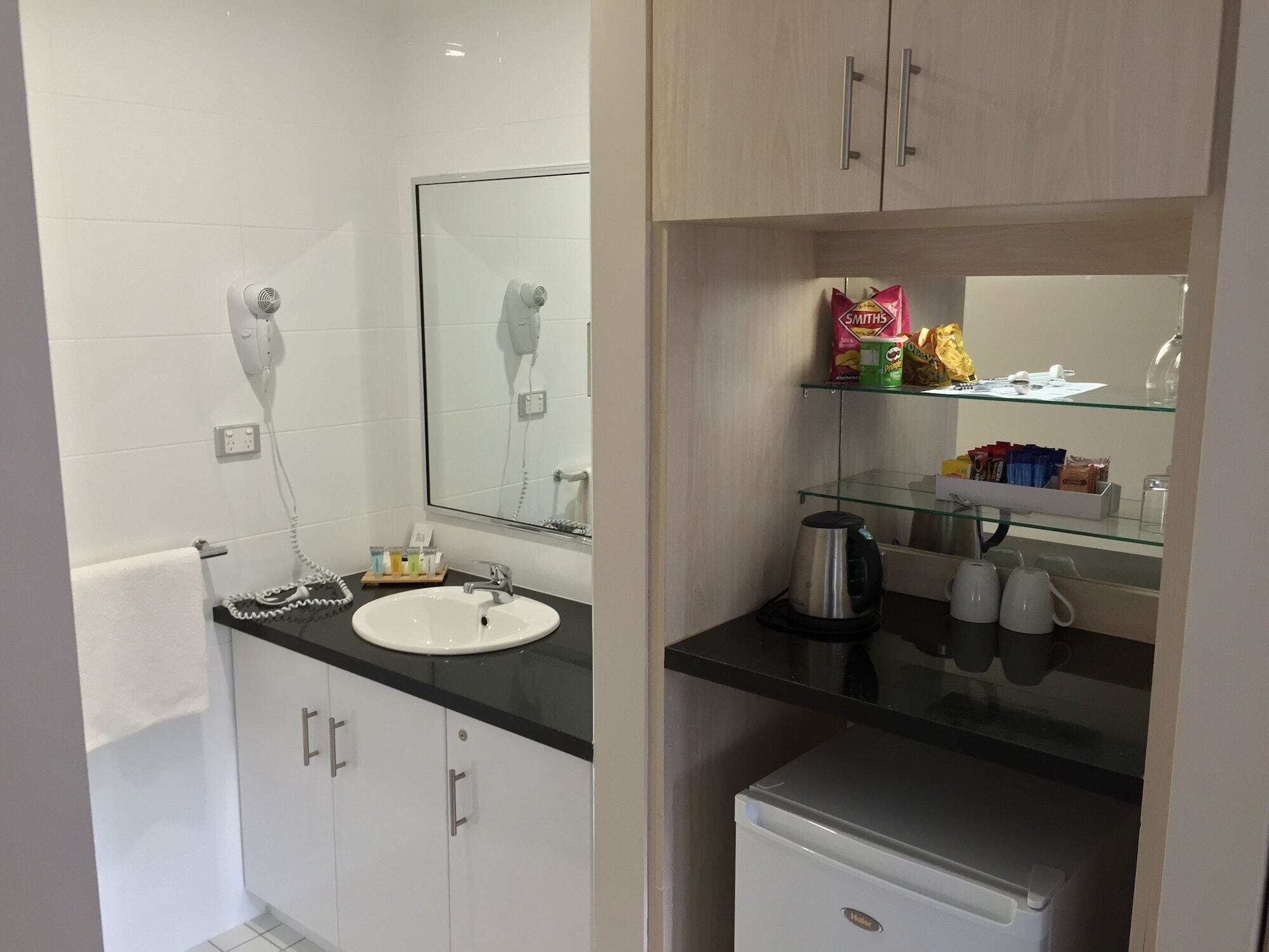 A modern bathroom with a sink, mirror, towel rack, and a small refrigerator.