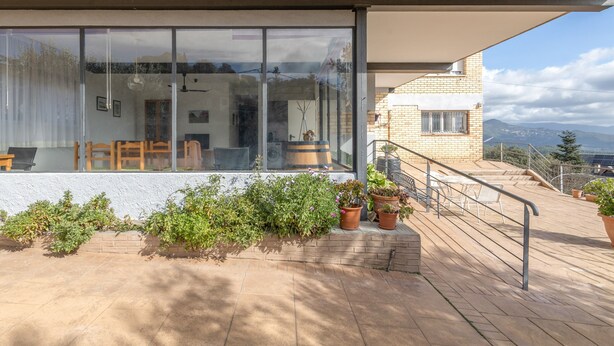 A modern building with large glass windows, a patio with potted plants, and a view of the mountains.