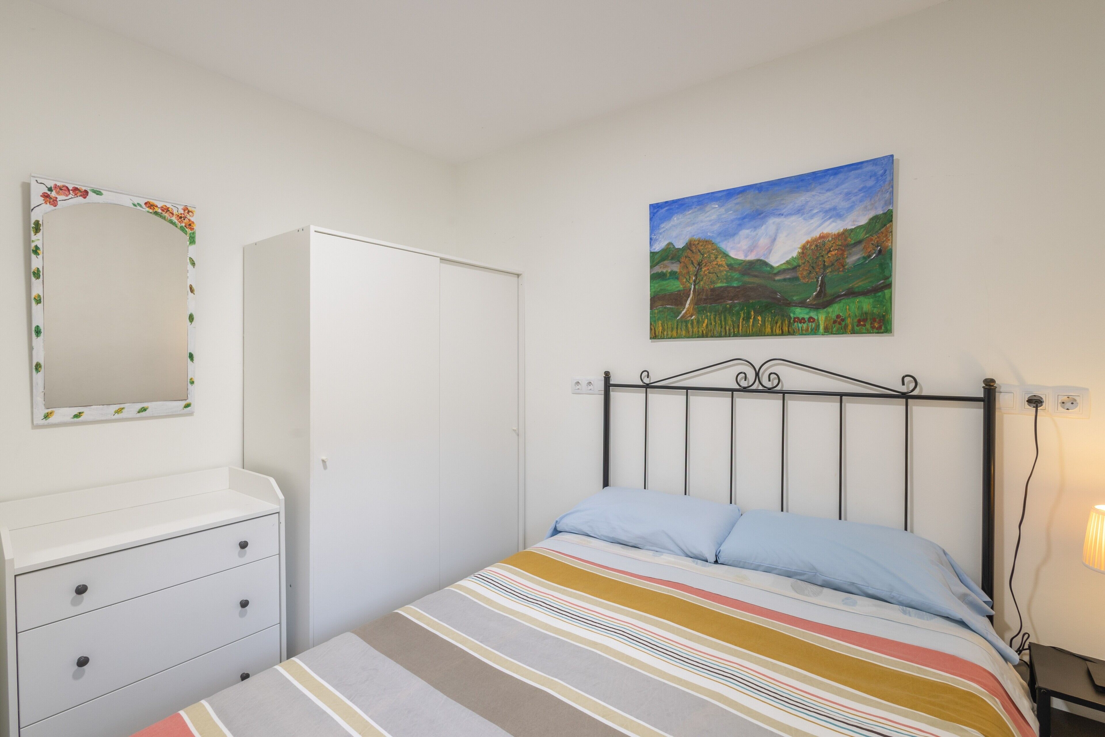 A bedroom with a bed, a dresser, a mirror, and a painting on the wall.