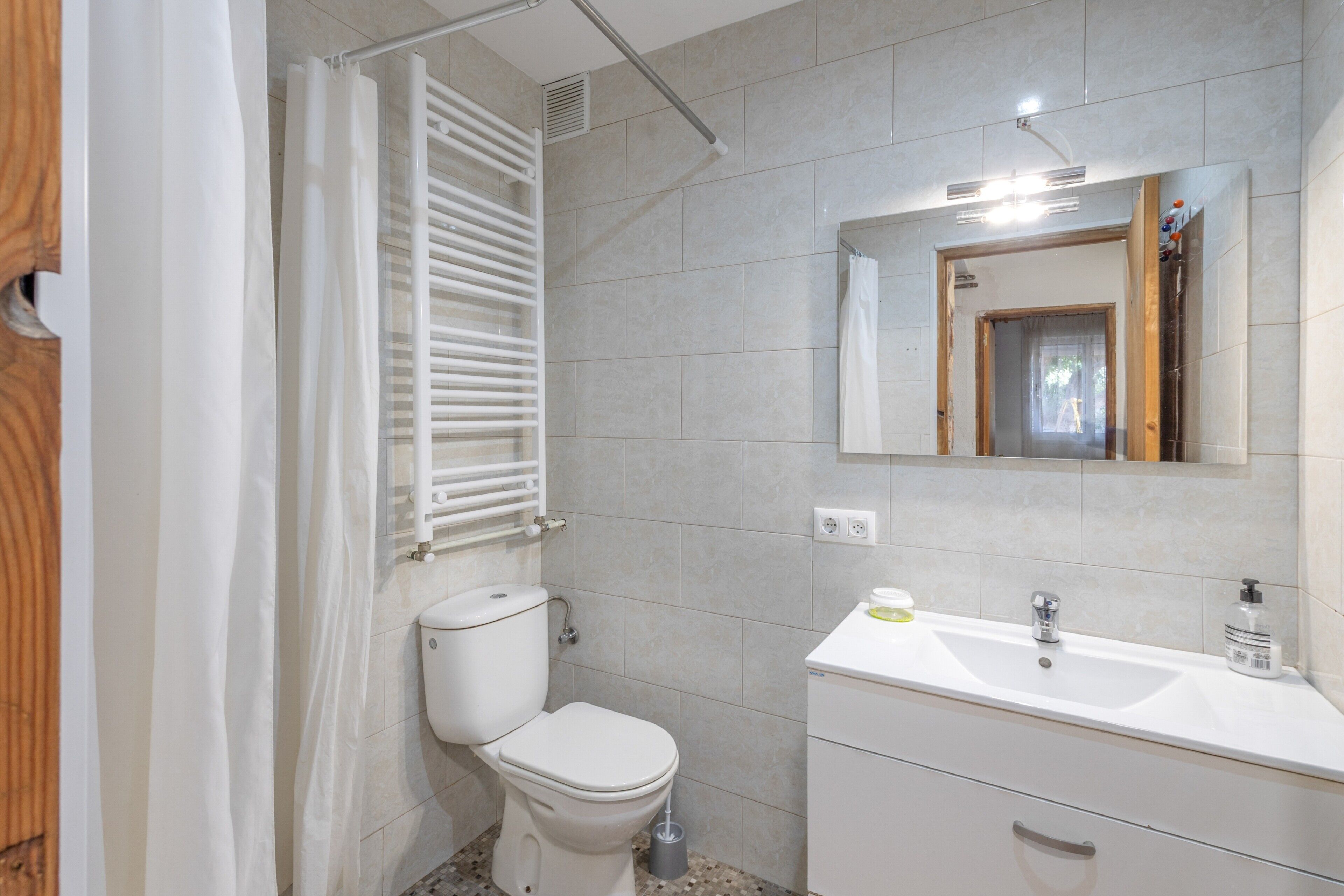 Uma casa de banho com sanita, lavatório, espelho e cortina de chuveiro.