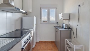 A compact kitchen with a stove, oven, and microwave, a small window with a view, and a white laundry basket.