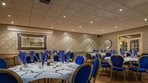 Une salle de banquet avec des tables rondes, des chaises bleues et des nappes blanches.