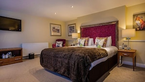 Une chambre d’hôtel avec un grand lit, un fauteuil rouge, une table d’appoint en bois, un téléviseur à écran plat fixé au mur et un tableau représentant un renard.