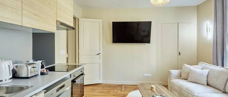 A modern kitchen with built-in appliances, a dining area with a wooden table, and a living room with a sofa and a flat-screen TV.