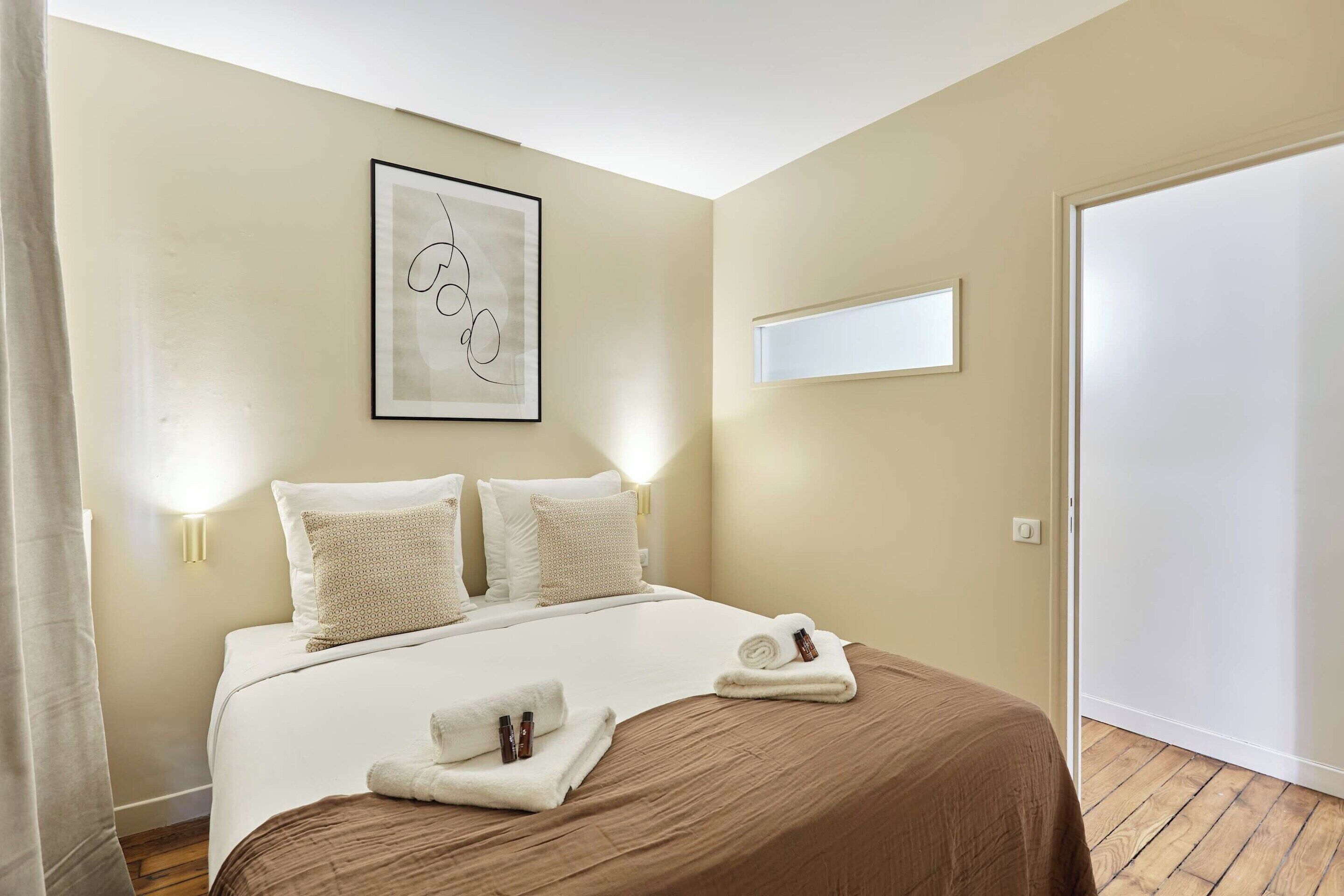 Een hotelkamer met een bed, twee bedlampen, een lijst met kunstwerk en een deur.
