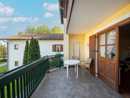 Un balcón con mesa y sillas, una puerta de madera y vista a un edificio cercano.