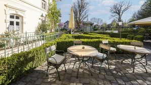 An outdoor café with tables and chairs, surrounded by neatly trimmed hedges and a building with classical architecture. - Grosszugiges Studio in Bad Birnbach (Bad Birnbach)