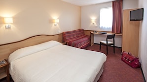 Une chambre d’hôtel avec un grand lit, un bureau, une chaise, une télévision et un sac à main rouge.