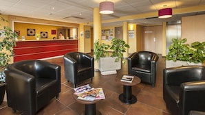 Un hall d’entrée avec un comptoir de réception, des fauteuils en cuir noir, une table basse avec des magazines et des plantes en pot.