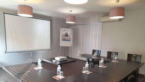 Une salle de conférence équipée d’une longue table, de chaises, d’un projecteur et d’un tableau blanc.