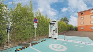 Une borne de recharge pour véhicules électriques, avec un panneau indiquant l’interdiction de se garer, un radar et un bâtiment en arrière-plan.