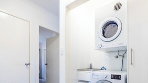 A laundry room with a front-loading washing machine and dryer, a small countertop, and a door leading to another room. - Blue Dolphin Holiday Resort (Yamba)