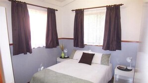 A bedroom with a bed, a bedside table, a lamp, and curtains. - Blue Dolphin Holiday Resort (Yamba)