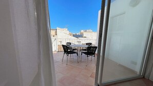 Un balcon avec une table et des chaises, un ciel bleu dégagé et des bâtiments en arrière-plan.