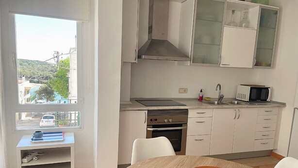 Une cuisine moderne avec des meubles blancs, un four à micro-ondes et une cuisini ère. Une fenêtre offre une vue sur un paysage verdoyant.