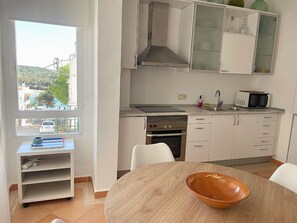 A modern kitchen with white cabinets, a microwave, and a stove. There's a window with a view of a green landscape. - Charming 2-bedroom apartment with AC in Portocolom (Felanitx)