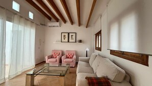 Un salon avec une table basse en verre, deux fauteuils roses, un canapé beige et un plaid rouge à carreaux.