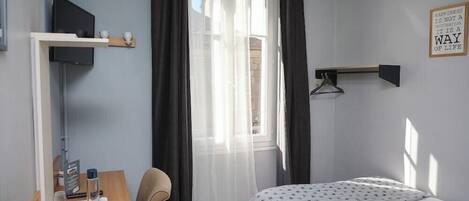 A hotel room with a bed, a desk, a chair, a TV, and a window with curtains.