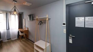 A room with a desk, chair, hanging clothes rack, and a door with a sign.