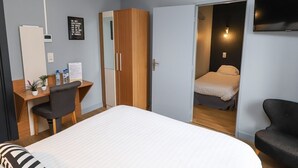 A hotel room with a bed, a desk with a chair, a wardrobe, and a TV.