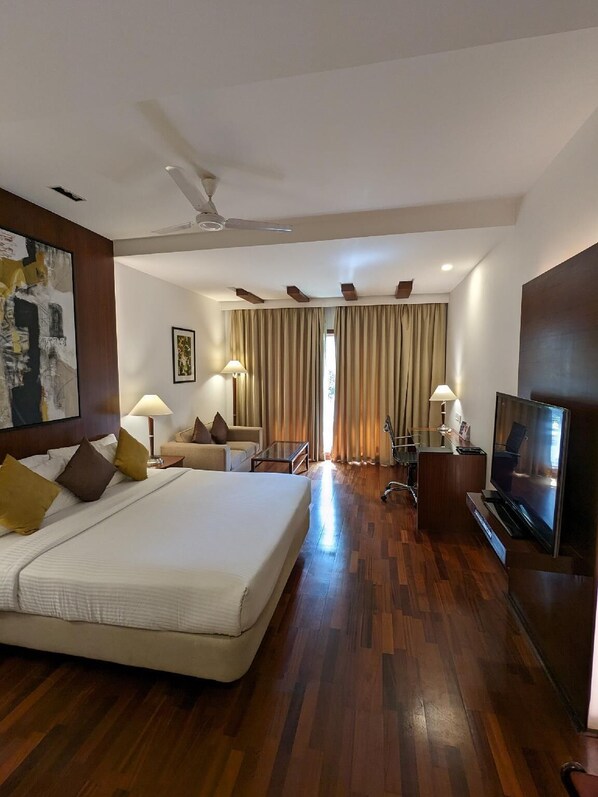 A hotel room with a large bed, a TV, a desk, and a chair. - Palm Meadows Resort (Bengaluru)