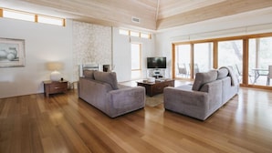 Un salón amplio con suelo de madera, dos sofás grises, un televisor de pantalla plana y un ventanal que proporciona luz natural.