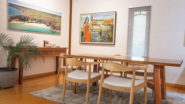 Un comedor con una mesa y sillas de madera, una planta en maceta y dos cuadros en la pared.