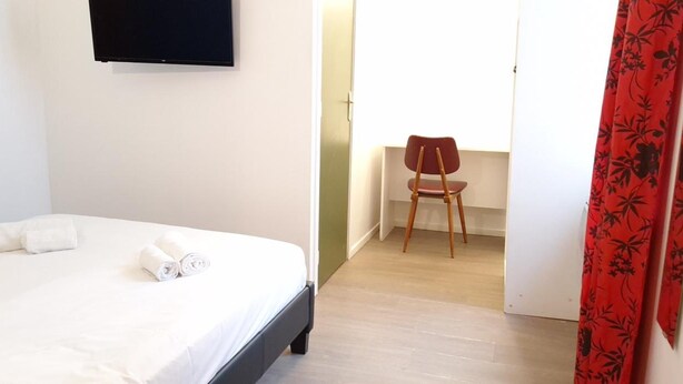 A hotel room with a bed, a chair, and a door with a red curtain.