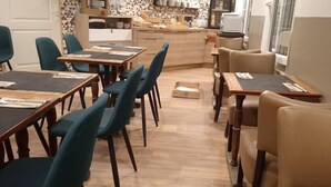 A dining area with tables and chairs, a kitchen in the background, and a view of the outside.