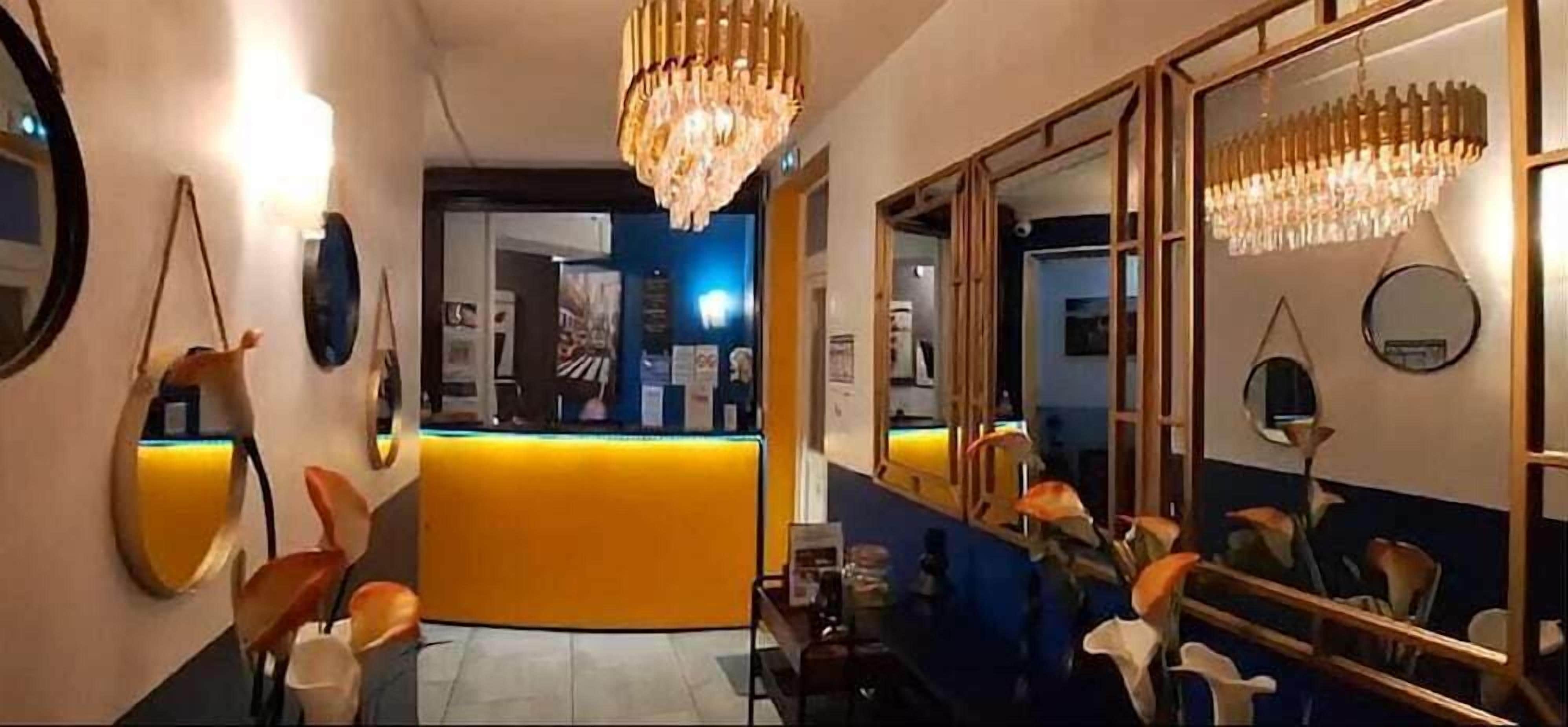 A hotel lobby with a reception desk, a large mirror, and a chandelier.