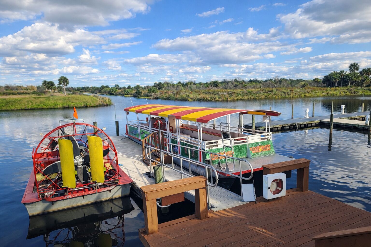 Een rivierboot aangemeerd aan een steiger, met een overdekt zitgedeelte en een klein houten platform.