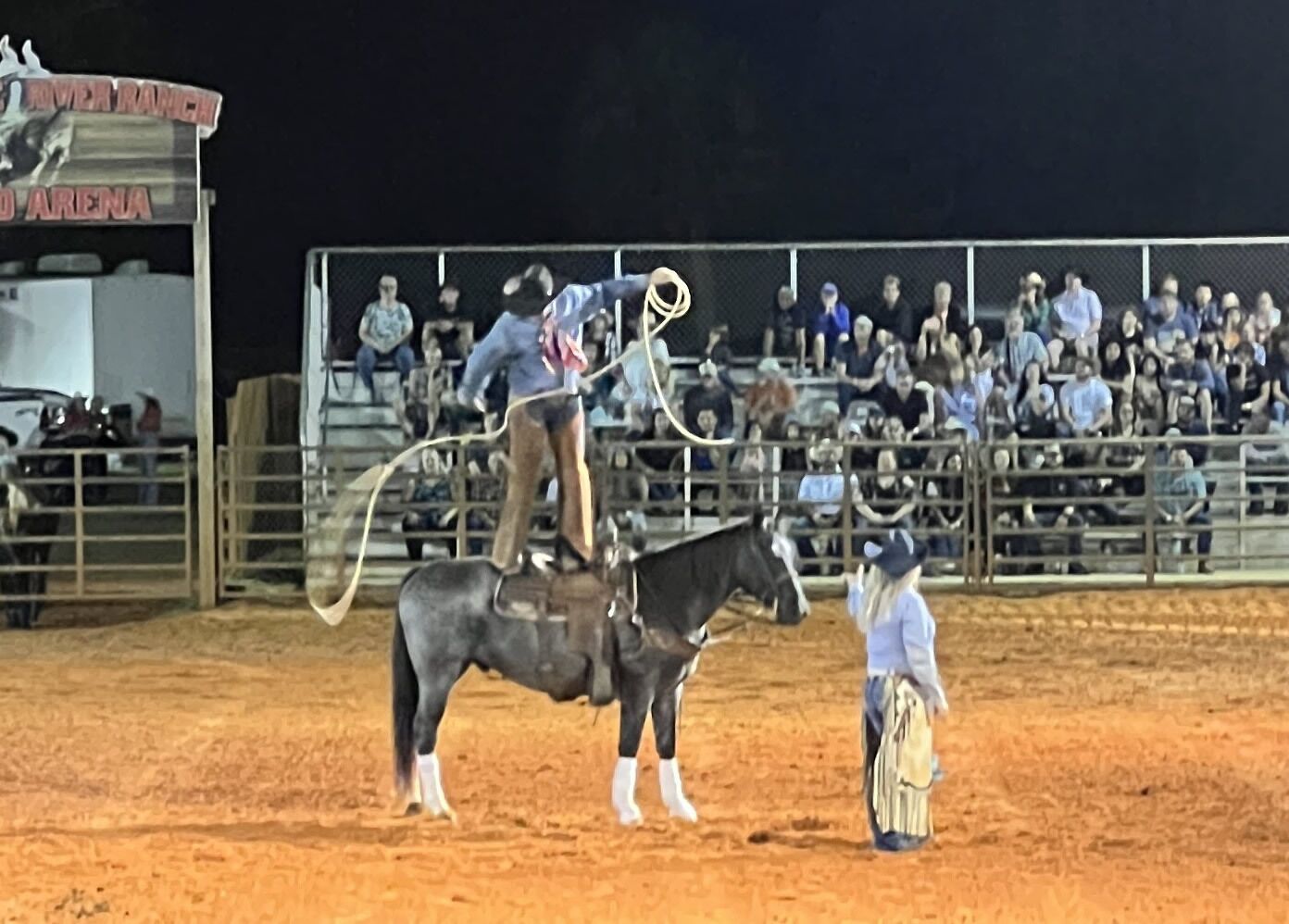 A rodeo event with a rider on a horse, an audience in the background, and a rodeo arena.