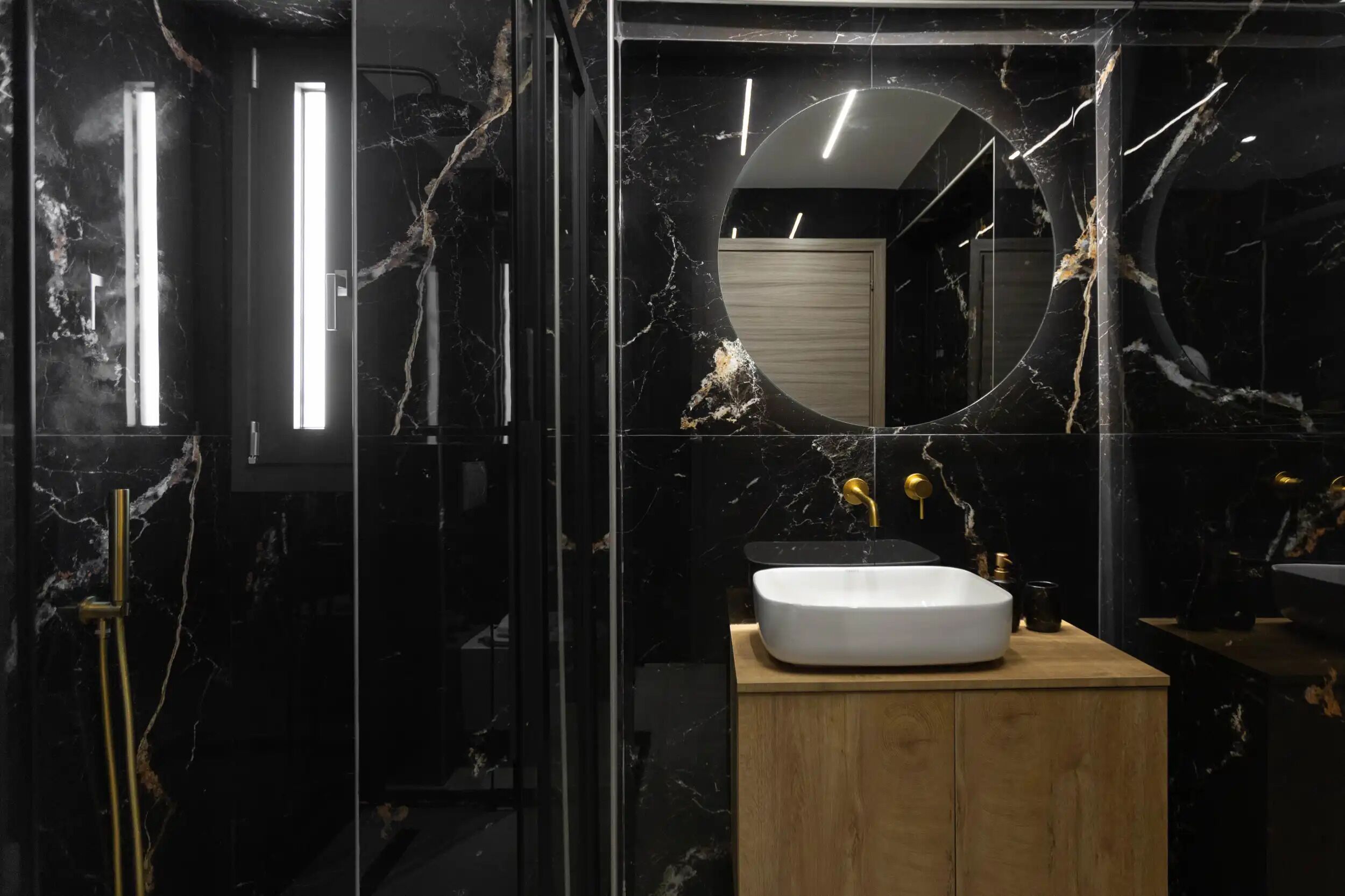 A modern bathroom with a marble vanity, a round mirror, and a glass-enclosed shower.