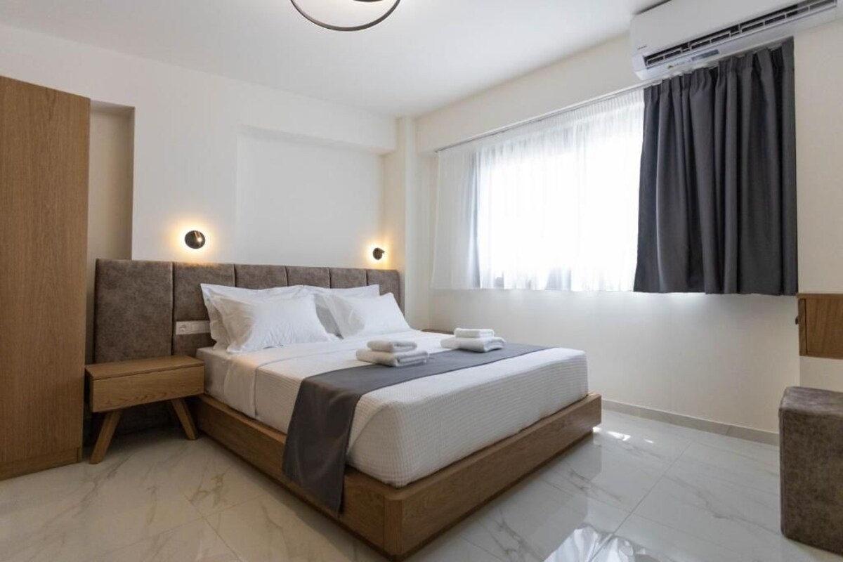 A modern hotel room with a large bed, bedside tables, a wardrobe, and a window with curtains.
