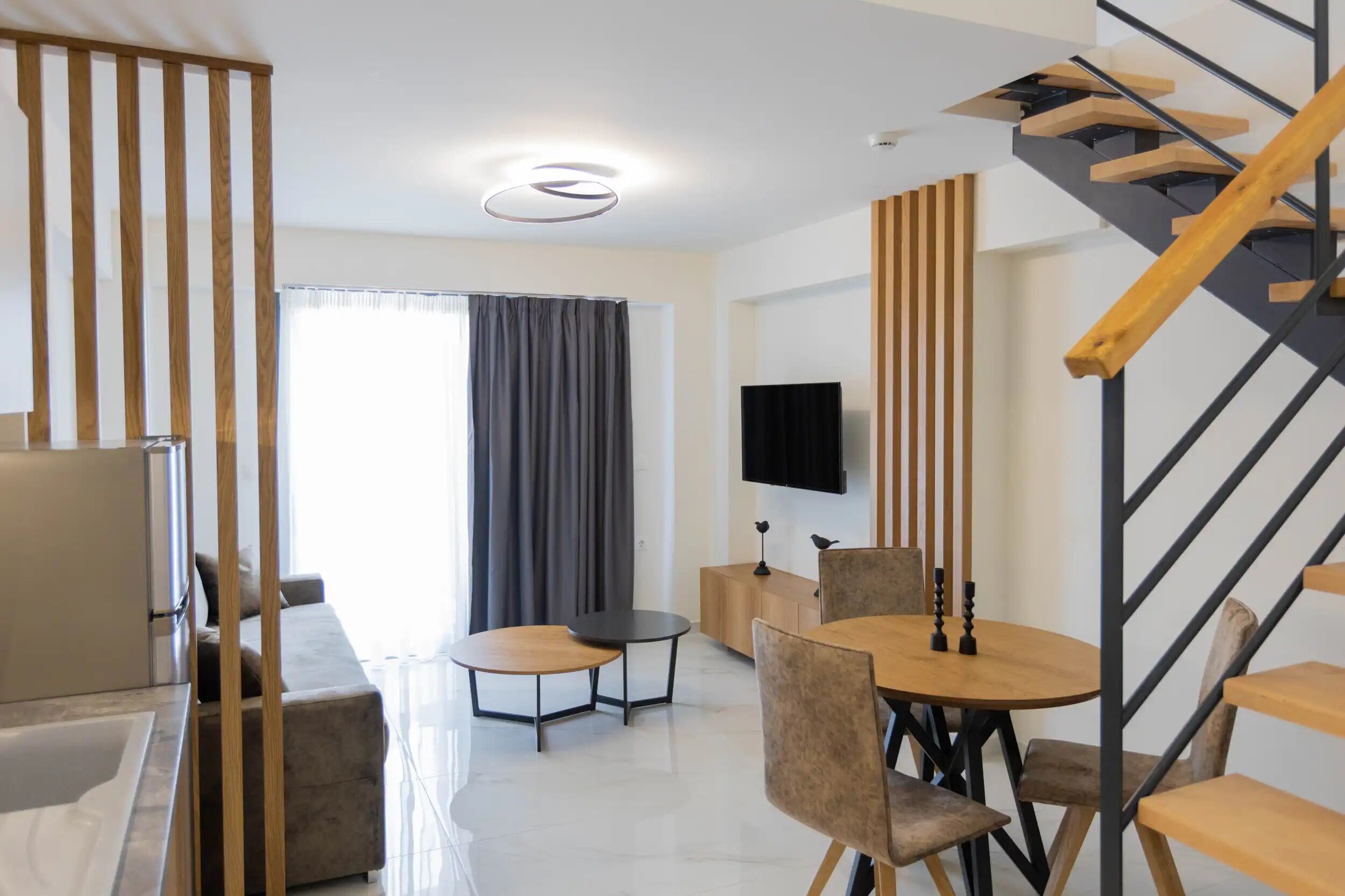 Ein modernes Wohnzimmer mit einer Couch, einem runden Holztisch und einem an der Wand befestigten Fernseher.