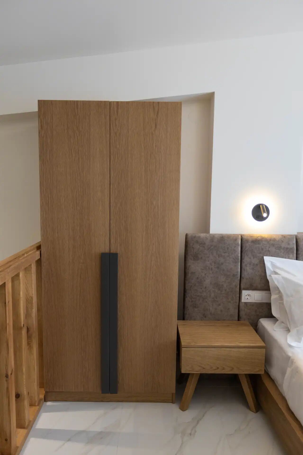 Habitació amb un armari de fusta, una taula petita de fusta, un sofà i una làmpada penjada a la paret.