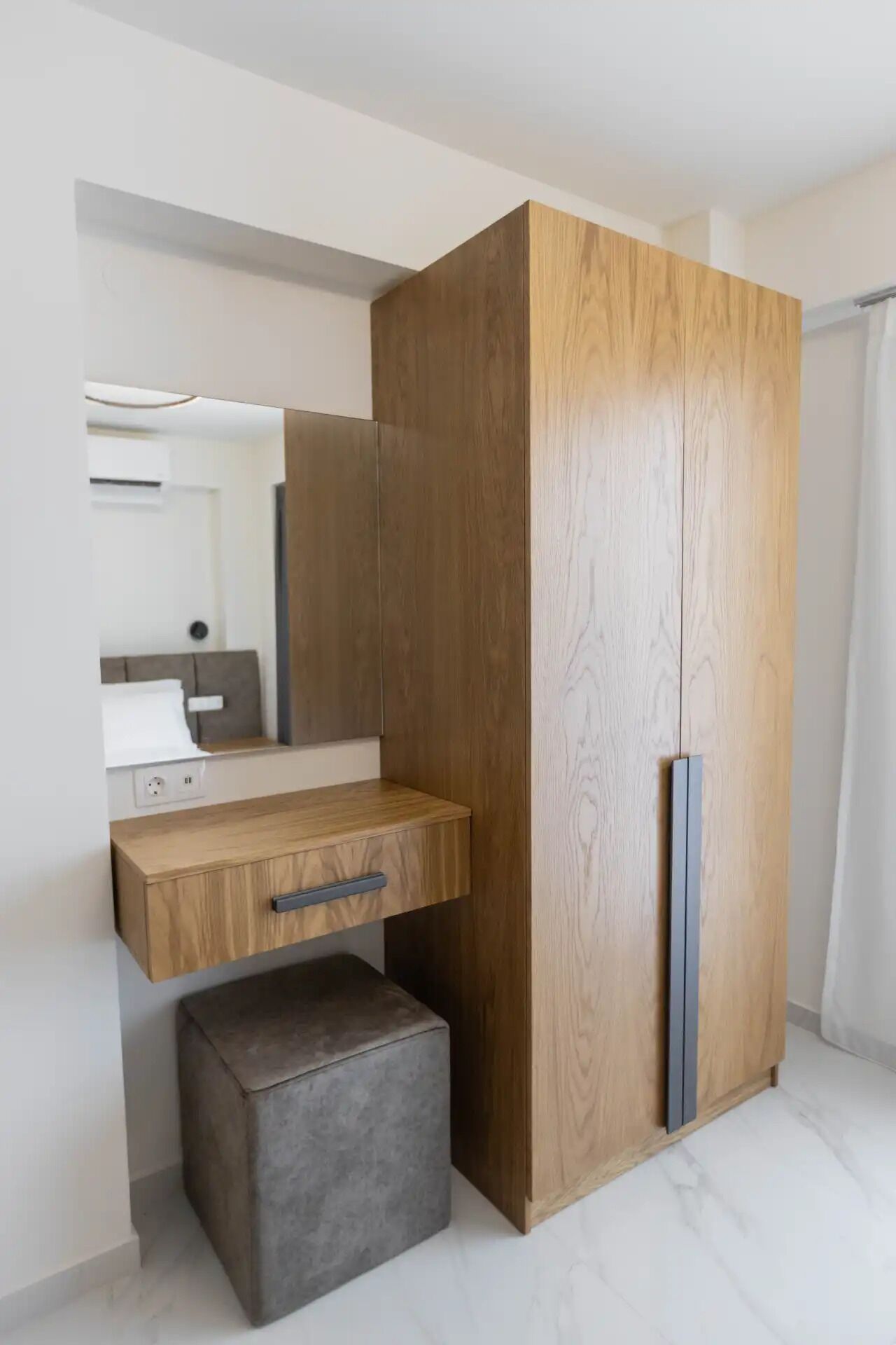 Un dormitorio moderno con un armario de madera, una mesita de noche y un pequeño otoman.