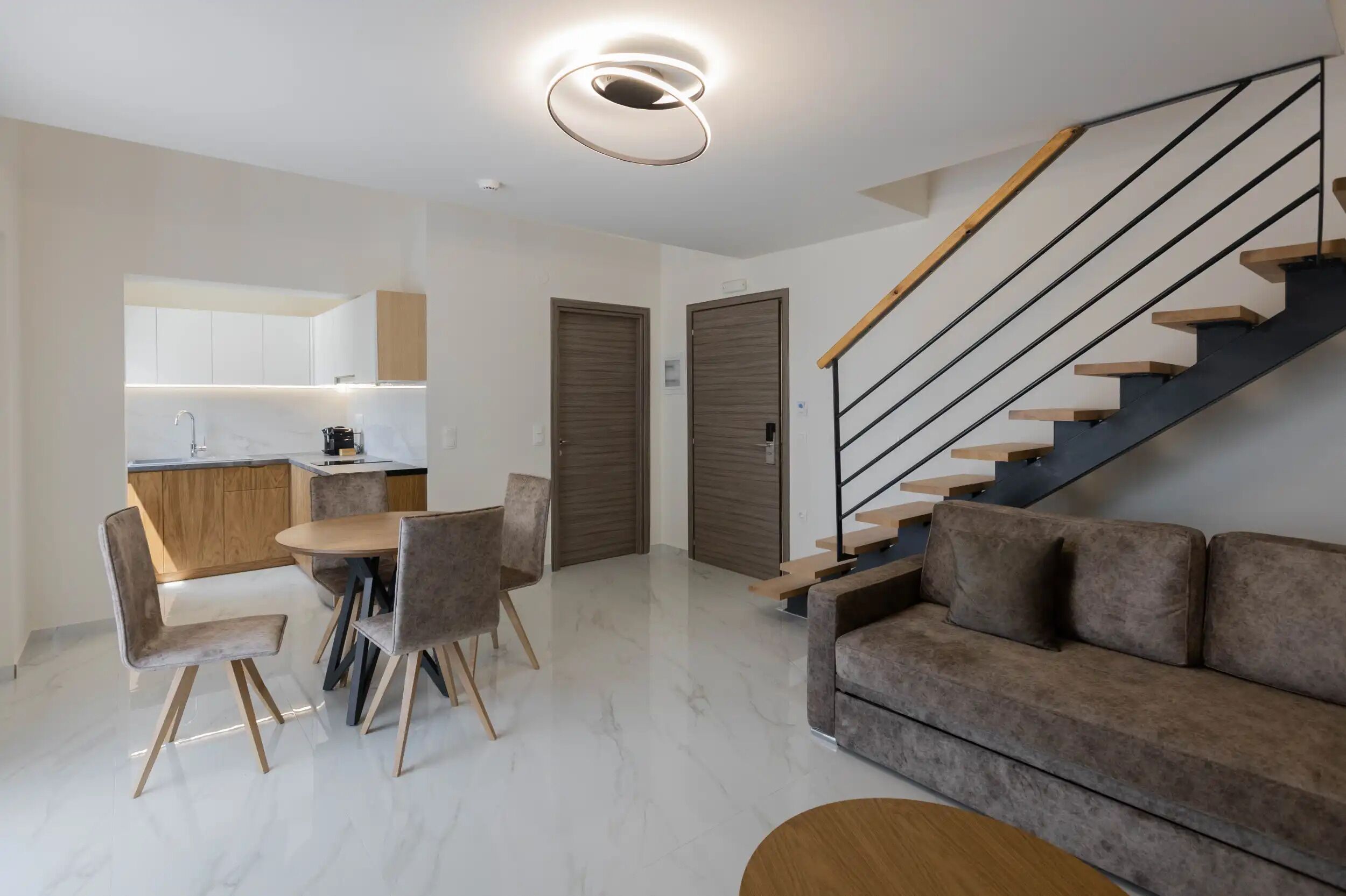 Uma sala de estar moderna com sofá, mesa de jantar, cadeiras, escada e área de cozinha.
