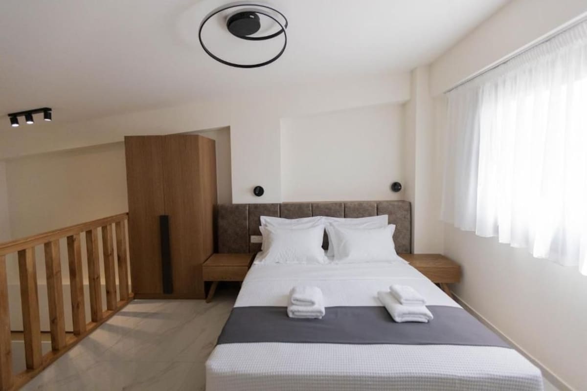 A modern hotel room with a bed, a wooden wardrobe, a nightstand, and a window with curtains.