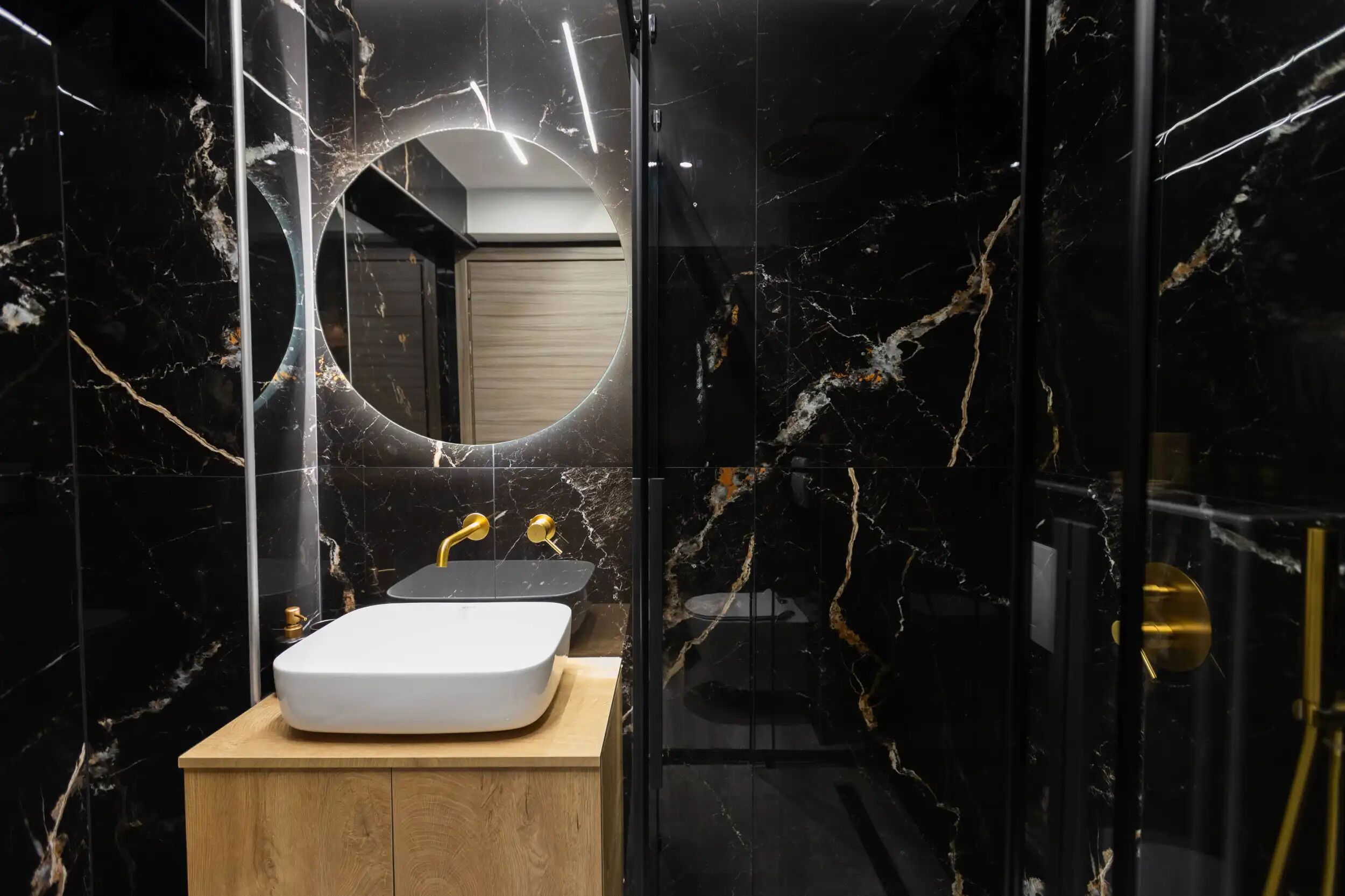 Een moderne badkamer met een marmeren wastafel, gouden details en een douchecabine met glazen wanden.