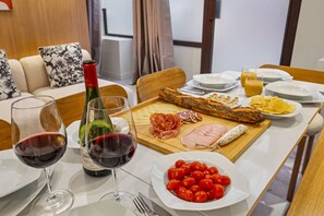 Ett matbord dukat med vinglas, en vinflaska, ett urval av ostar, charkuterier, en baguette, körsbärstomater och en tallrik med pommes frites.