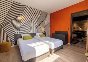 Et moderne hotelværelse med to senge, en væg med geometrisk mønster og en accentvæg i orange.