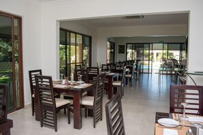 A dining area with multiple tables and chairs, large windows, and a view of the outdoors. - Twangale Park (Lusaka)