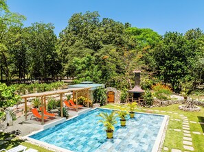 A swimming pool with a stone structure, a wooden pergola, and a stone fireplace surrounded by lush greenery. - Buendía Lux • Villa Harmonia. Stunning 3 king beds with pool near the beach. (Potrero)
