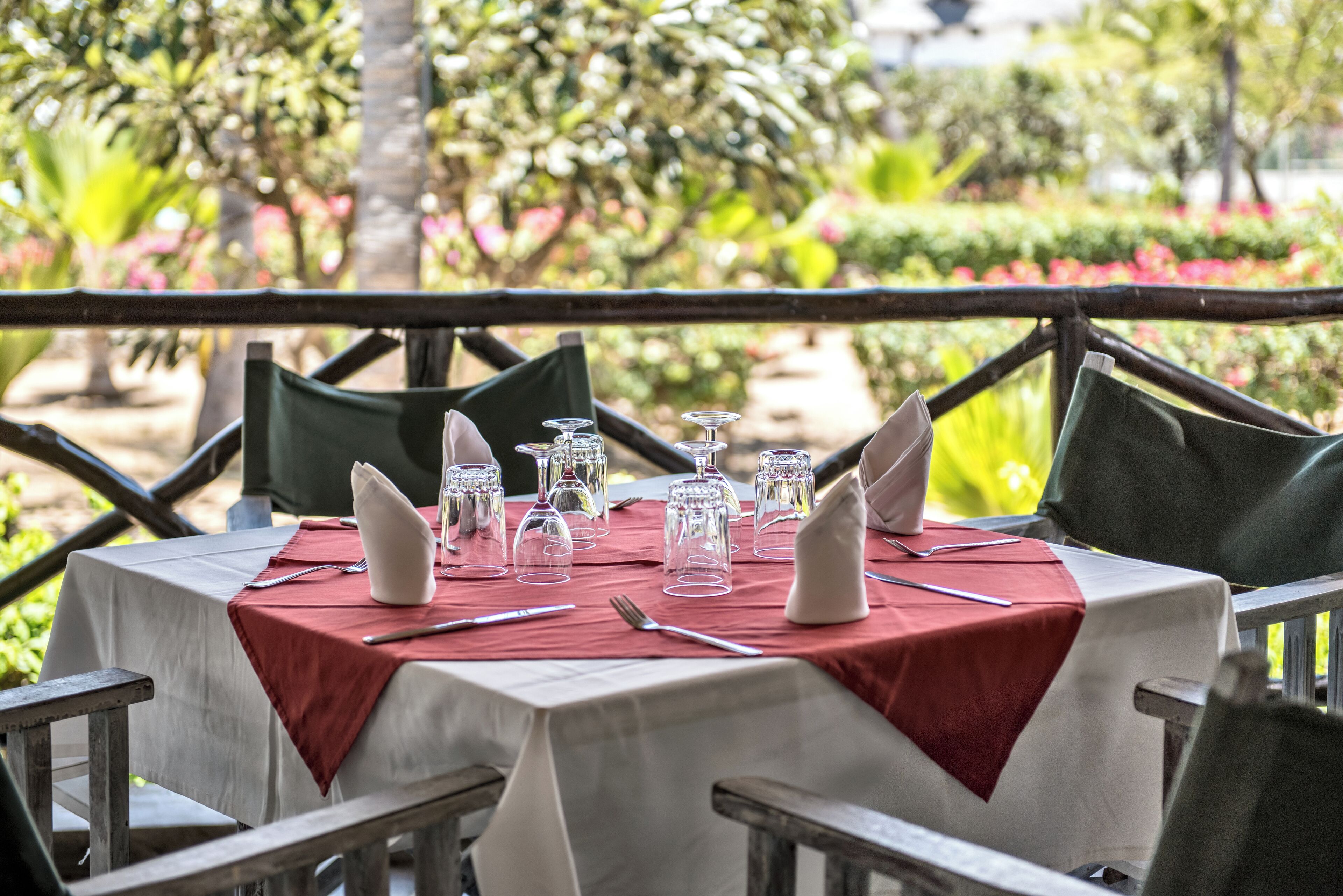 A table set outdoors with a red tablecloth, white napkins, and clear drinking glasses.