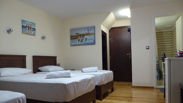 Una habitación de hotel con tres camas de madera, ropa de cama blanca y dos cuadros en las paredes.