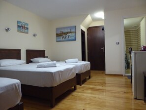 A hotel room with three wooden beds, white linens, and two paintings on the walls. - The Sea Front Rooms and Apartments (Rethymno)